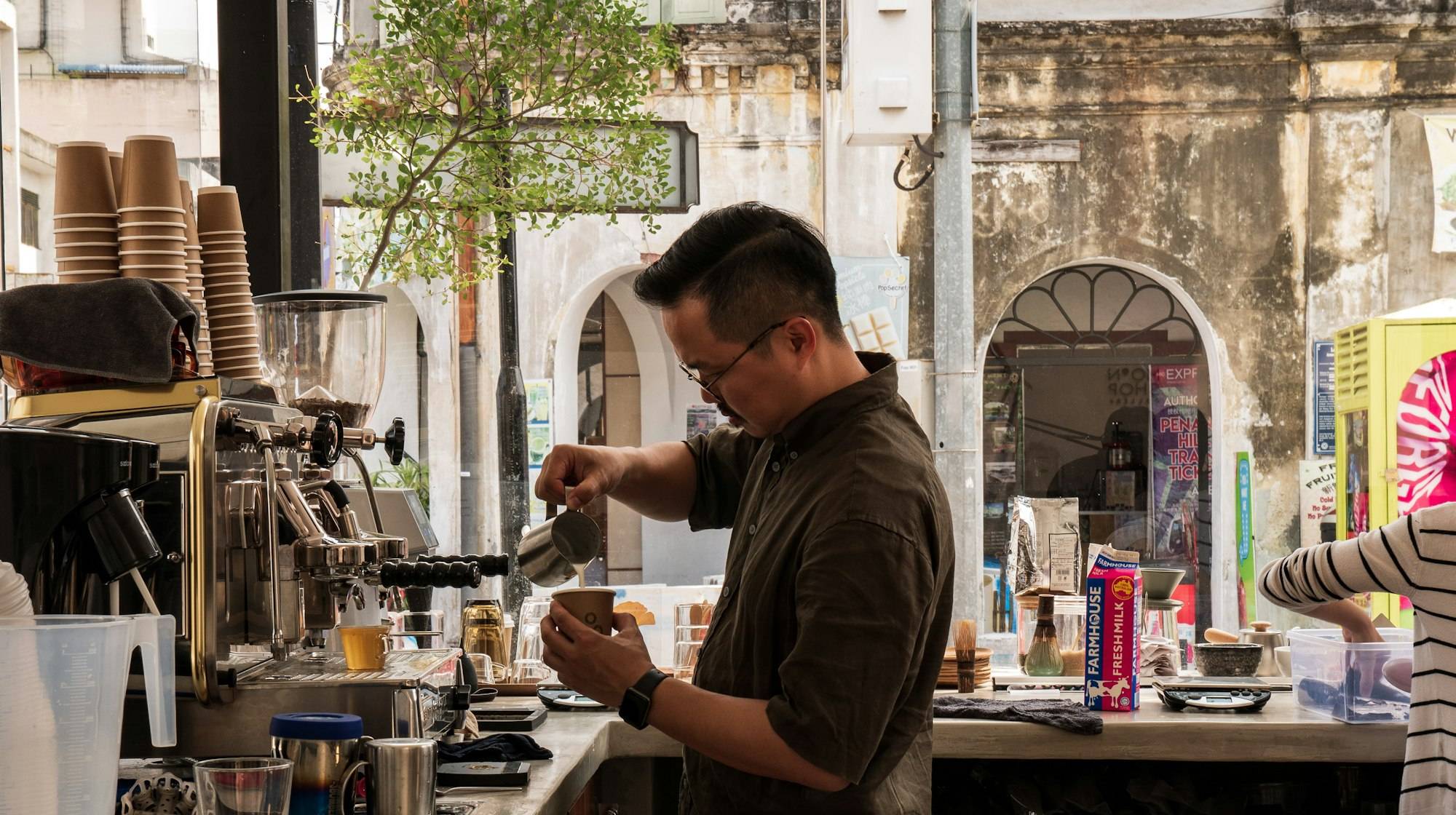 A barista pouring steamed milk into a takeaway cup at a coffee counter
